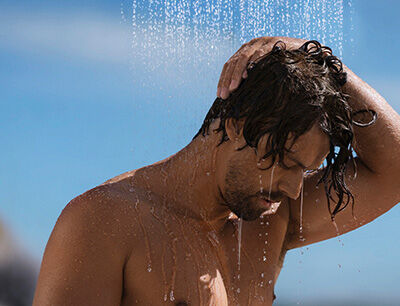 Mann steht unter der Dusche im Freien.