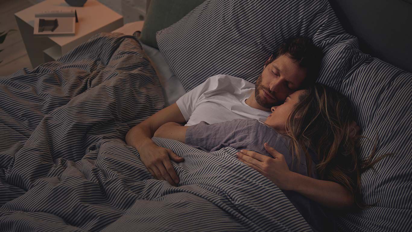 Couple sleeping arm in arm in bed.