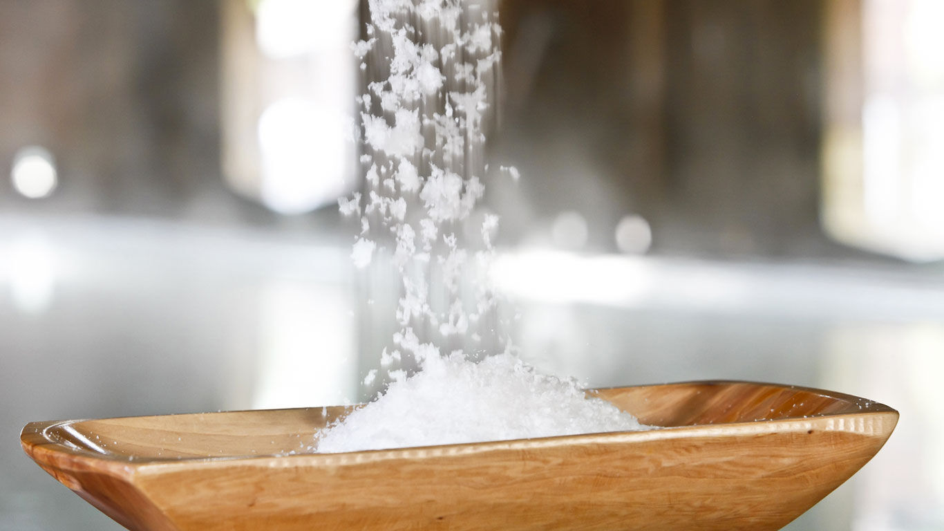 Natural deep salt trickles down into a wooden bowl.
