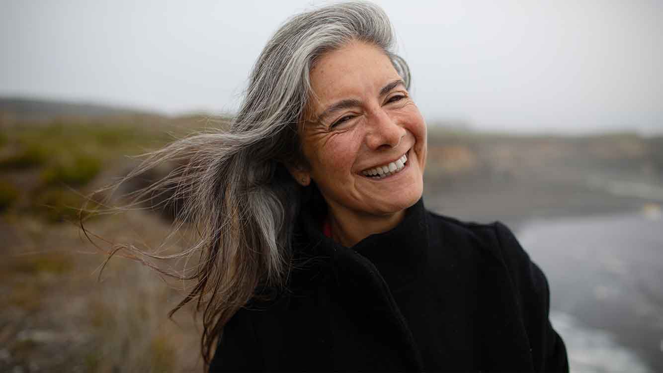 Frau mit langen grauen Haaren lächelt im Wind.