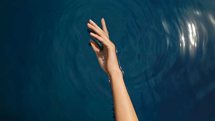 Ausgestreckte Hand liegt im Wasser.
