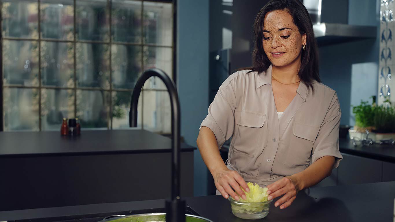 Frau wäscht Salat in der Küche. 