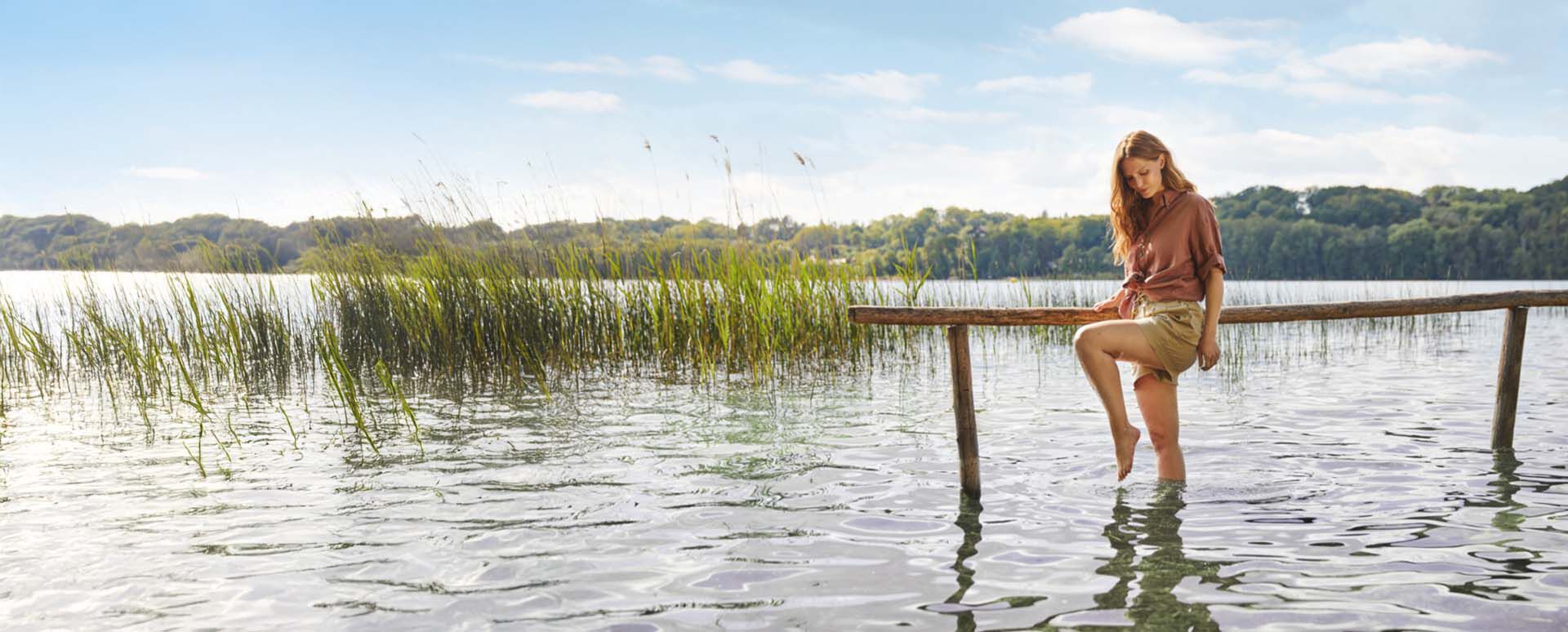 Frau l&auml;uft mit den F&uuml;&szlig;en durchs Wasser.