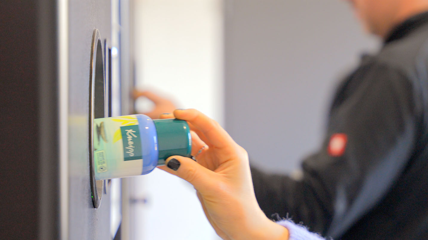 Frau schiebt eine Kneipp Schaumbadflasche in einen Pfandautomaten Frau schiebt eine Kneipp Schaumbadflasche in einen Pfandautomaten