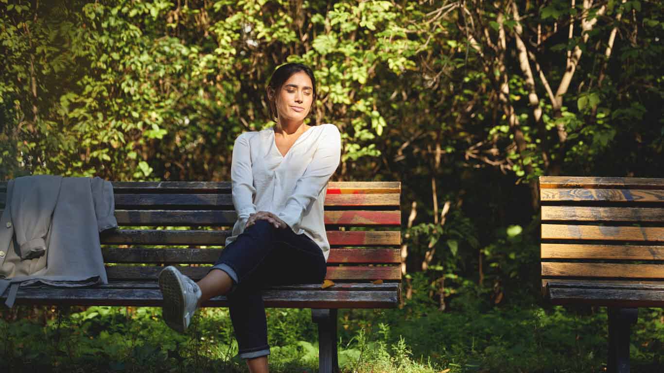 Frau sitzt auf einer Parkbank und genie&szlig;t die Sonne.