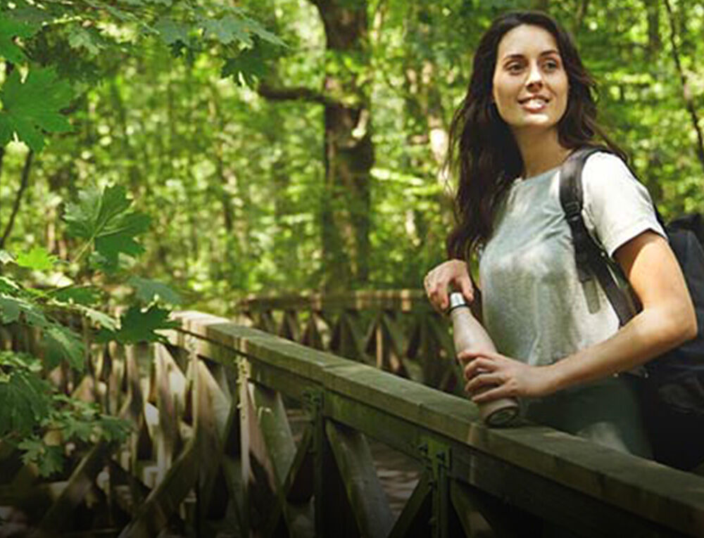 Frau beim Wandern im Wald mit einer Trinkflasche in der Hand.