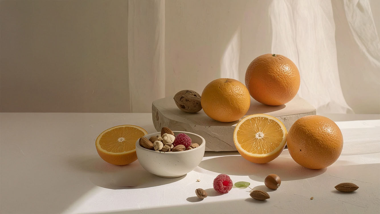 Frische Orangen mit N&uuml;ssen und Beeren auf heller Naturstein-Deko &ndash; gesundes Food-Arrangement.