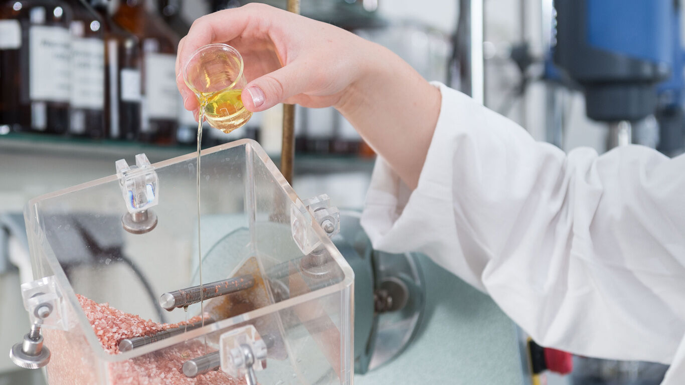 A woman pours vegetable oil over bath salts in the lab