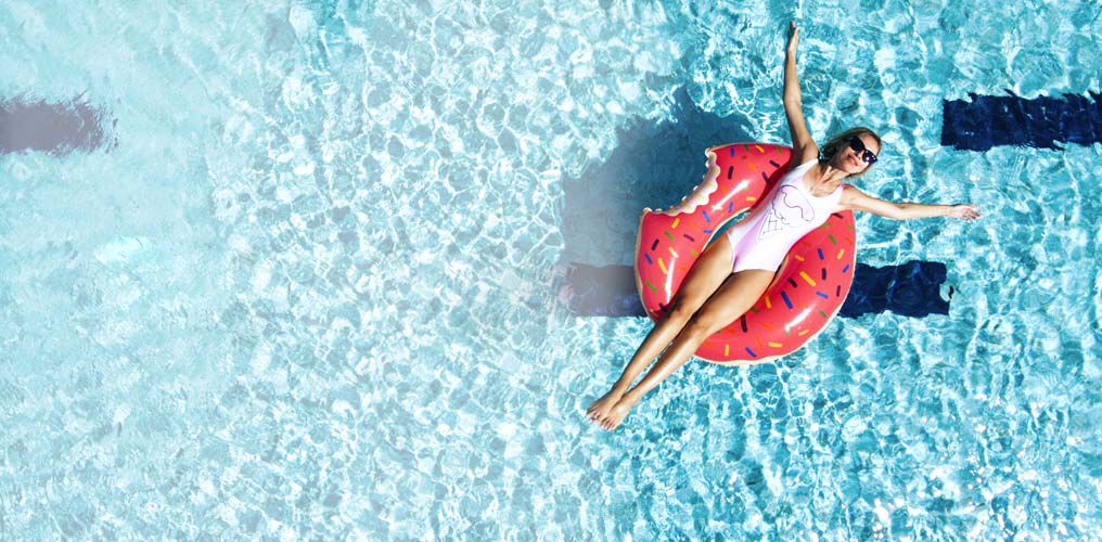 Frau in weißem Badeanzug auf einem Pinken Donut-Schwimmring im Wasser.