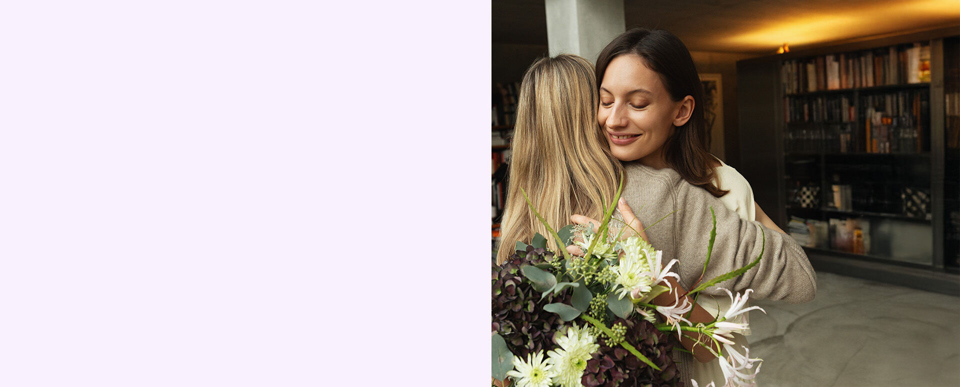 Zwei Frauen umarmen sich mit einen Blumenstrauß.