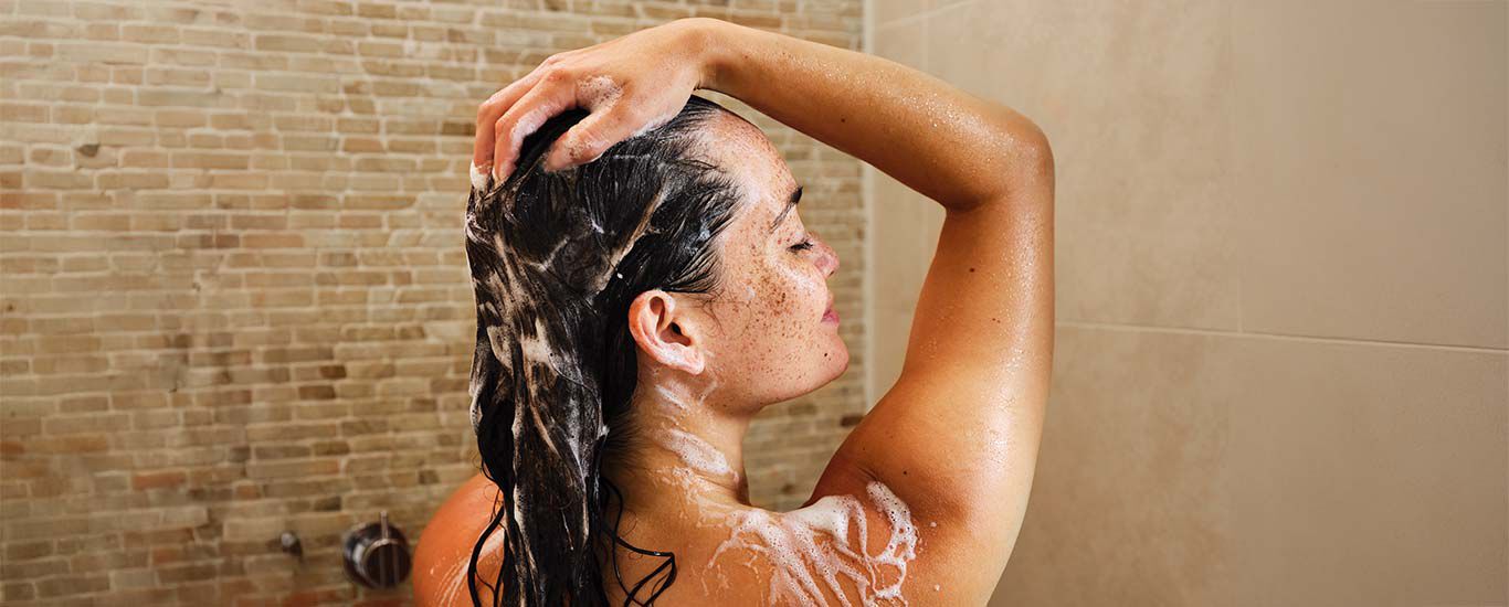 Frau steht unter der Dusche und wäscht Haare. 