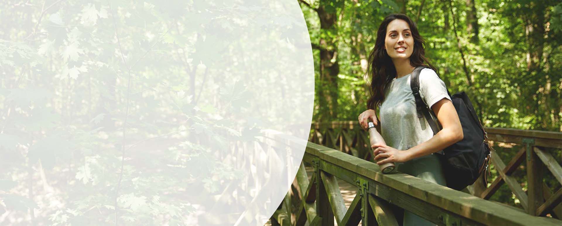 Frau beim Wandern im Wald mit einer Trinkflasche in der Hand.