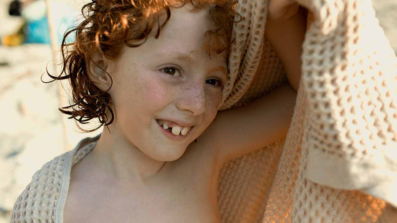 Junge mit Locken schützt sich mit einem Handtuch vor der Sonne. 