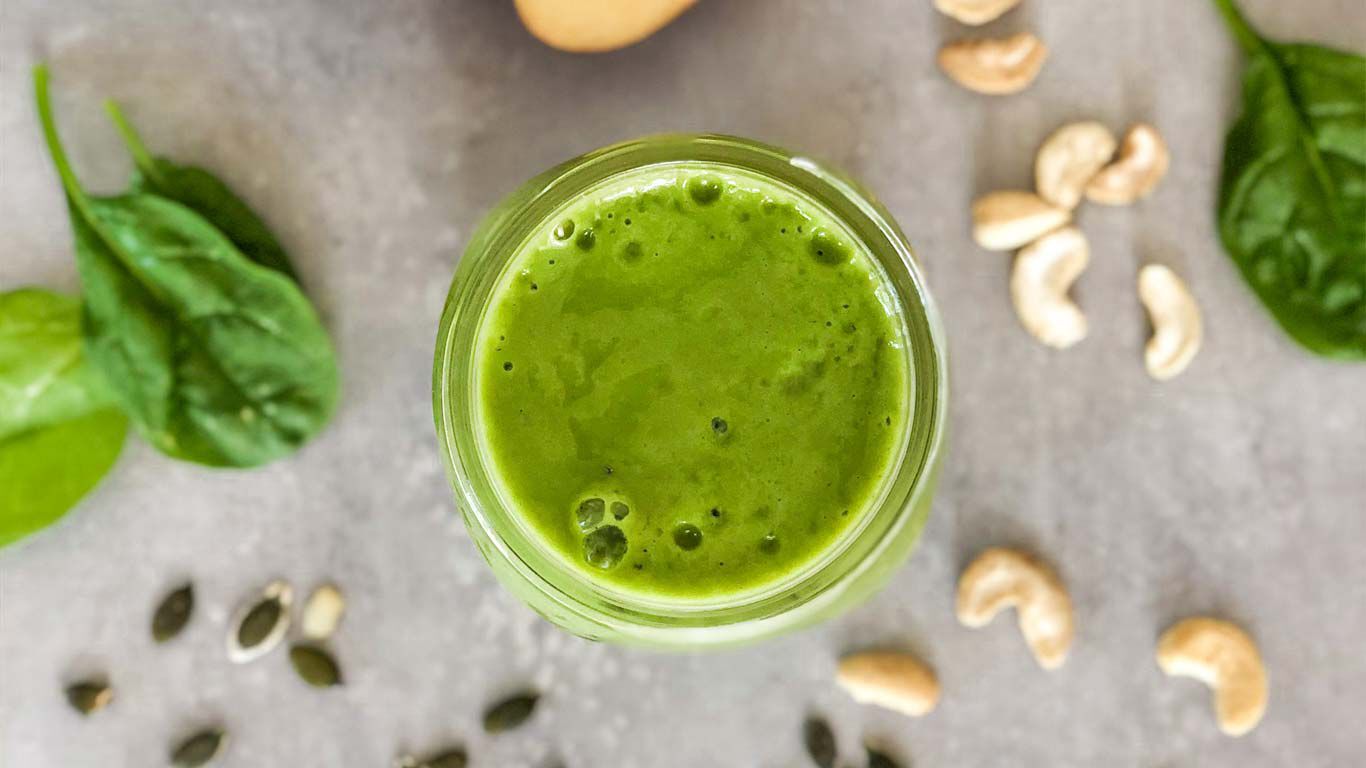 Top Ansicht eines grünen Smoothies mit Cashewnüssen und Kürbiskernen neben dem Glas.