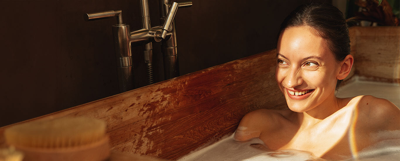 Frau sitzt in der Badewanne und wird von der Sonne angestrahlt. 