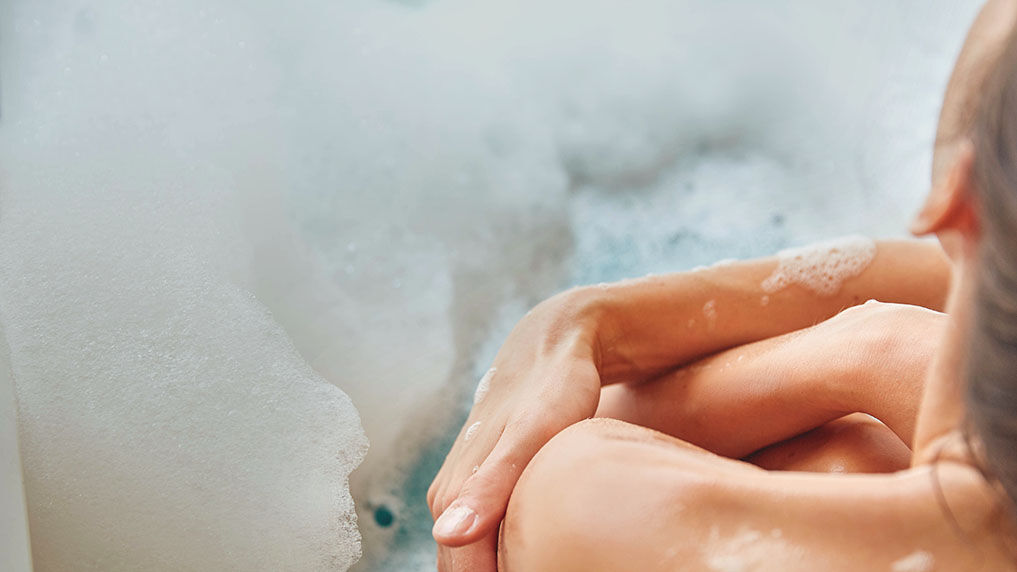 Frau sitzt in einer Badewanne mit Schaum. 