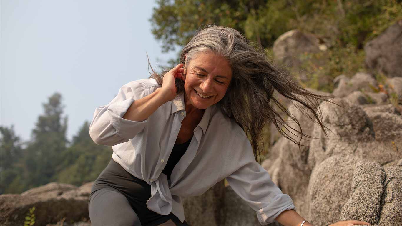 Frau klettert auf Felsen. Ihre Haare wehen im Wind.