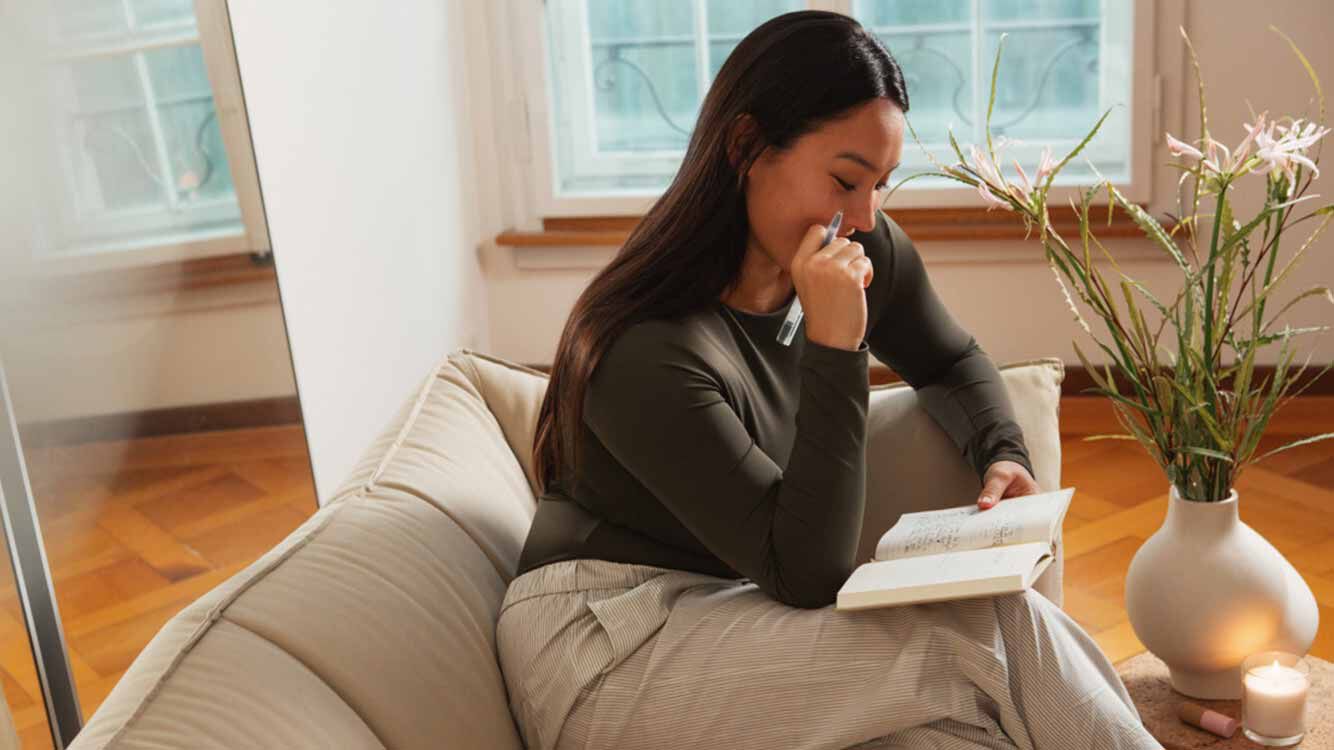 Frau sitzt mit Notizbuch und Stift auf dem Sofa und &uuml;berlegt.