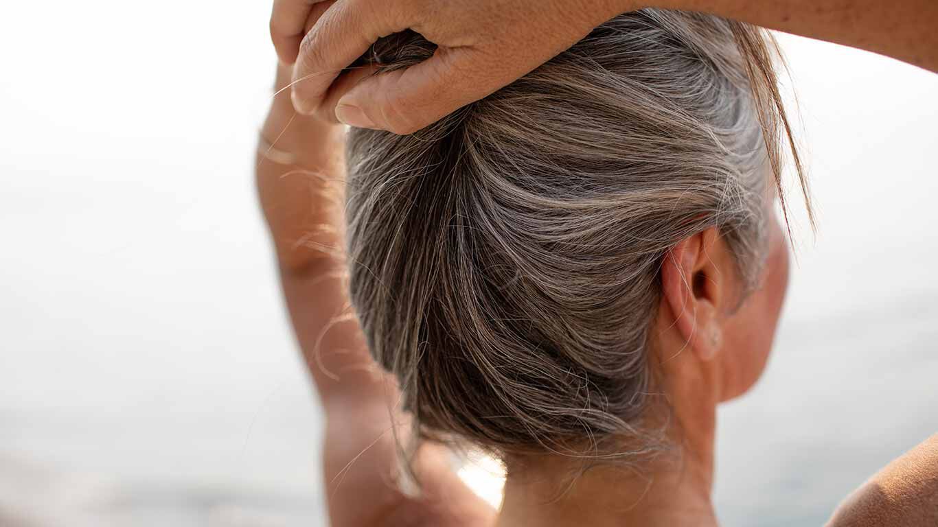 Rückansicht einer Frau, die ihre Arme über dem Kopf zusammennimmt.