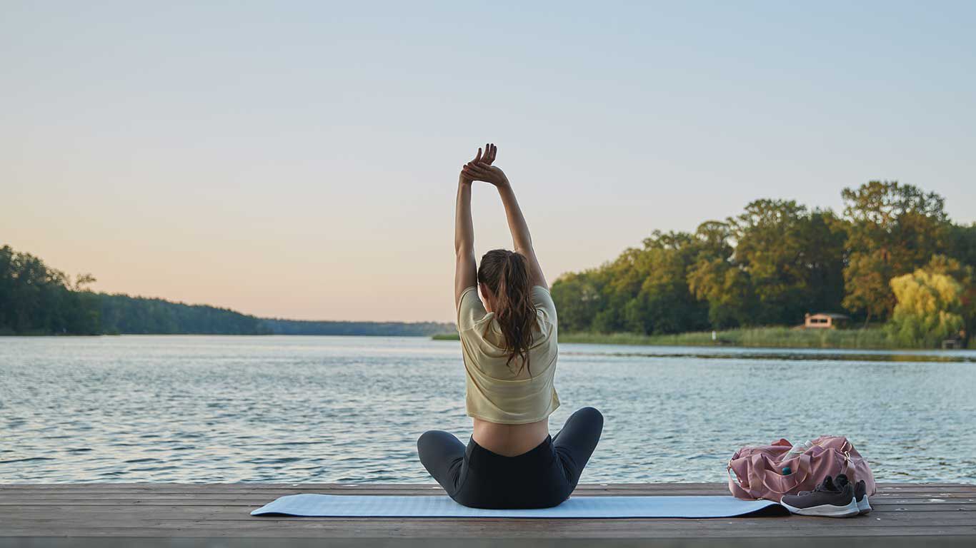 Frau im Schneidersitz auf einer Yogamatte auf einem Seesteg.