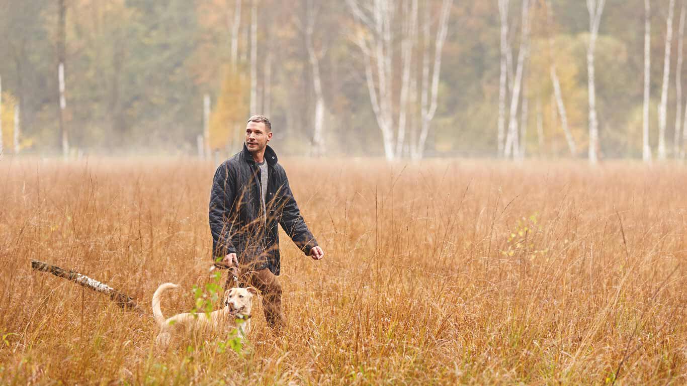 Mann spaziert mit Hund in der Natur.