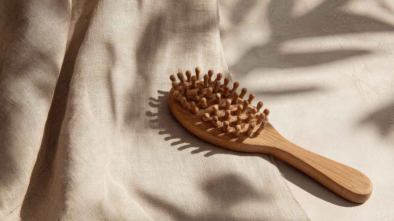 Holzb&uuml;rste mit runden Noppen liegt auf beigem Stoff, im Sonnenlicht mit Schatten von Bl&auml;ttern.