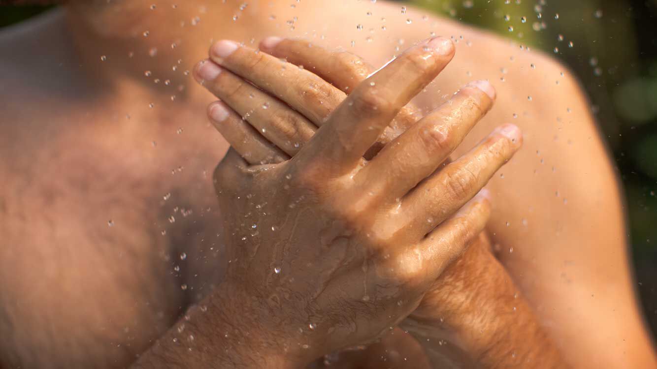 Nahaufnahme zweier Hände eines Mannes unter der Dusche. 