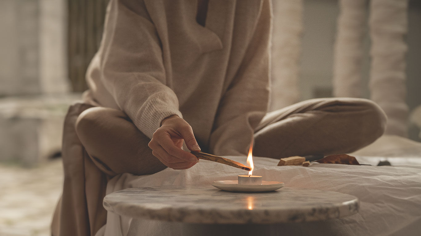 Frau im Schneidersitz zündet Palo Santo Holz über einem Teelicht an. 