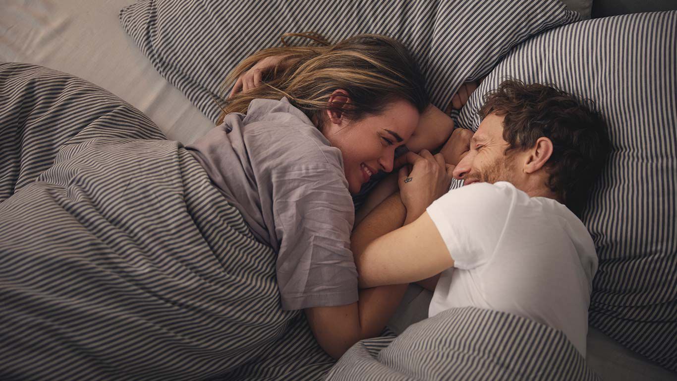 Couple lying in bed and smiling at each other. 