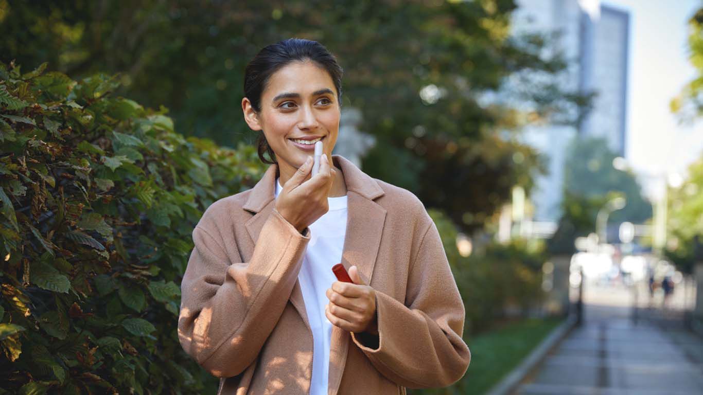 Frau läuft  auf einem Gehweg, umgeben von grünen Sträuchern und Bäumen, mit modernen Gebäuden im Hintergrund.