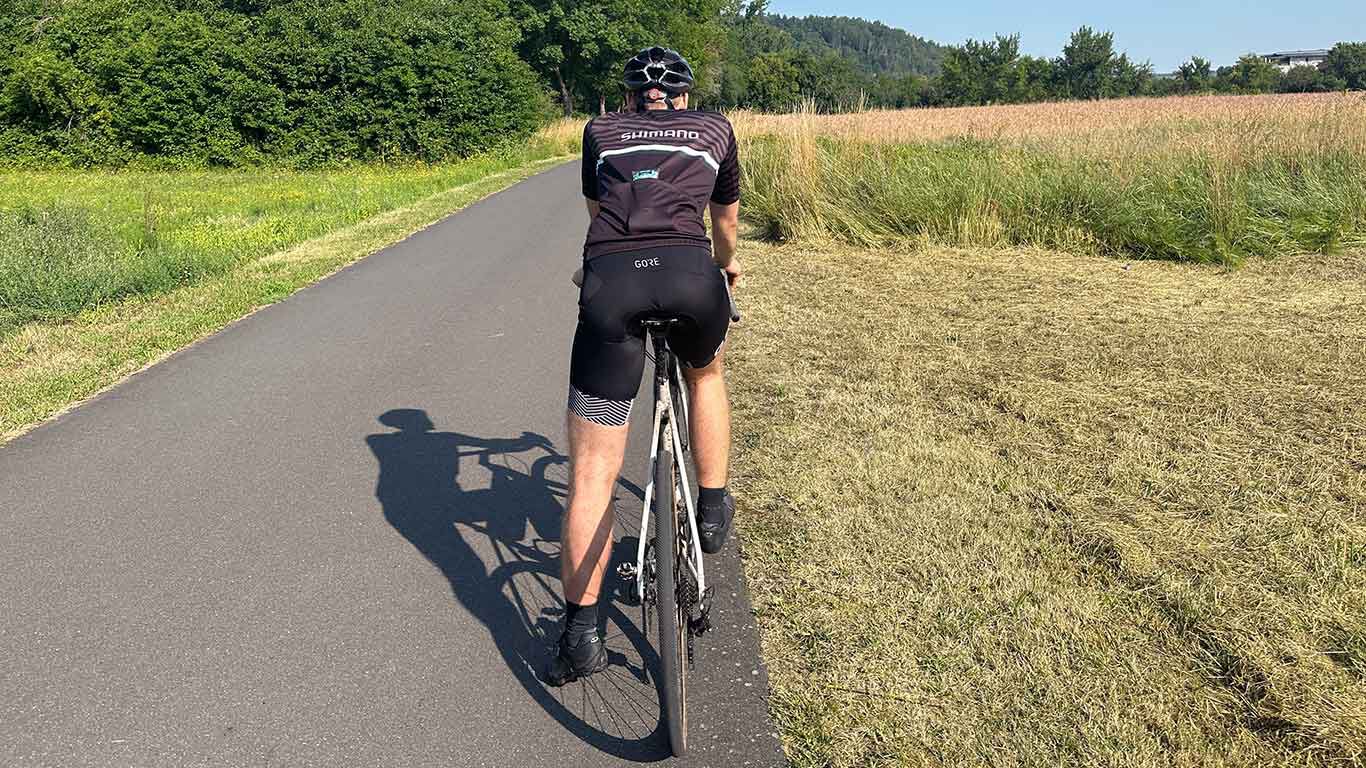 Frau mit langen, dunklen Haaren schiebt ihr Fahrrad durch die Stadt.