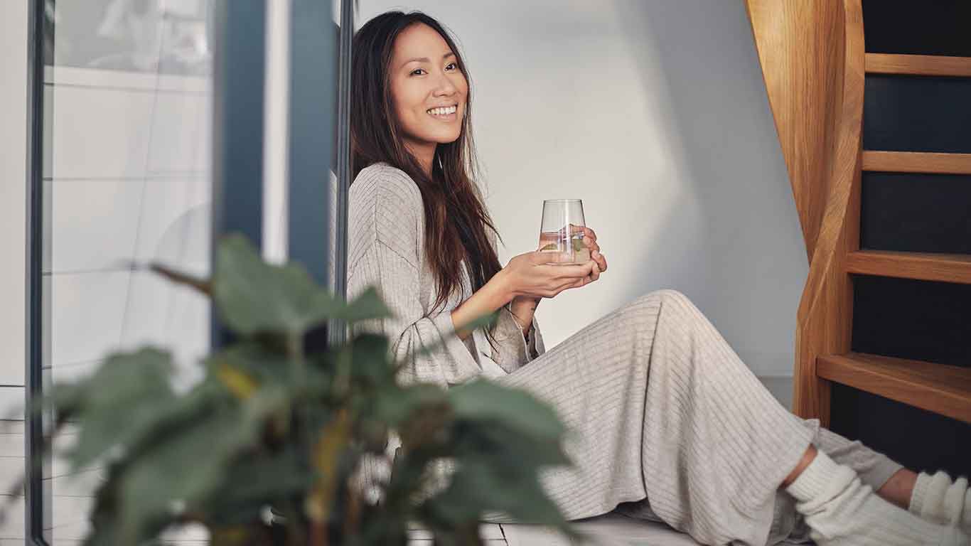 Frau sitzt mit einem Wasserglas in der Hand auf dem Boden. 