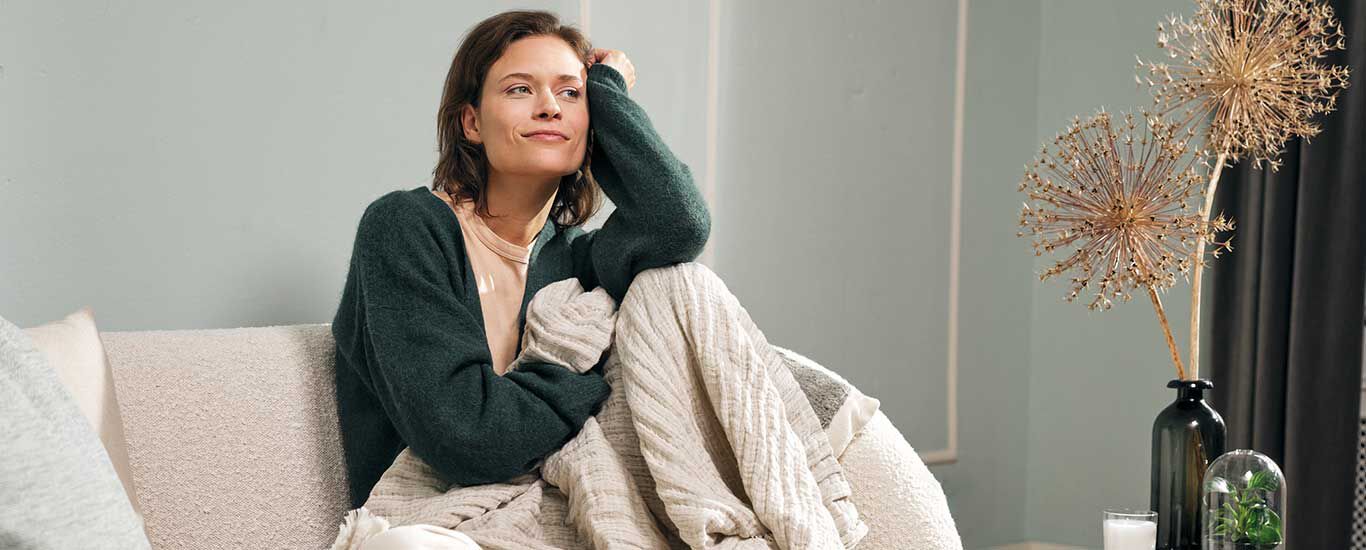 Frau sitzt auf der Couch und genießt Self-Care-Zeit.