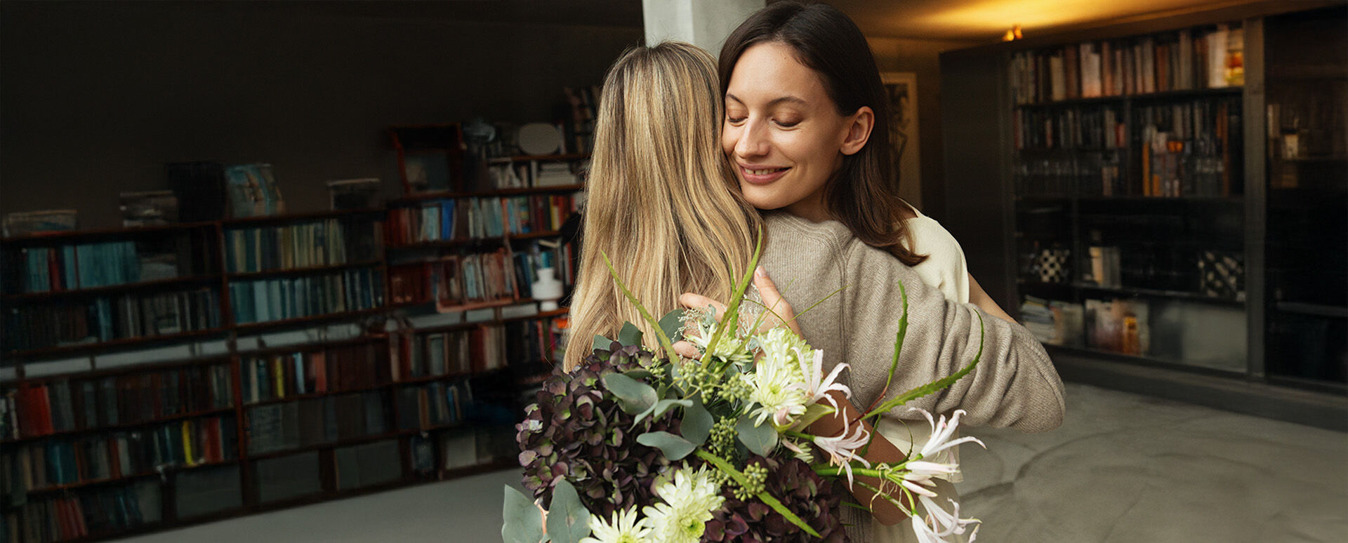 Zwei Frauen umarmen sich mit Blumenstrau&szlig;.