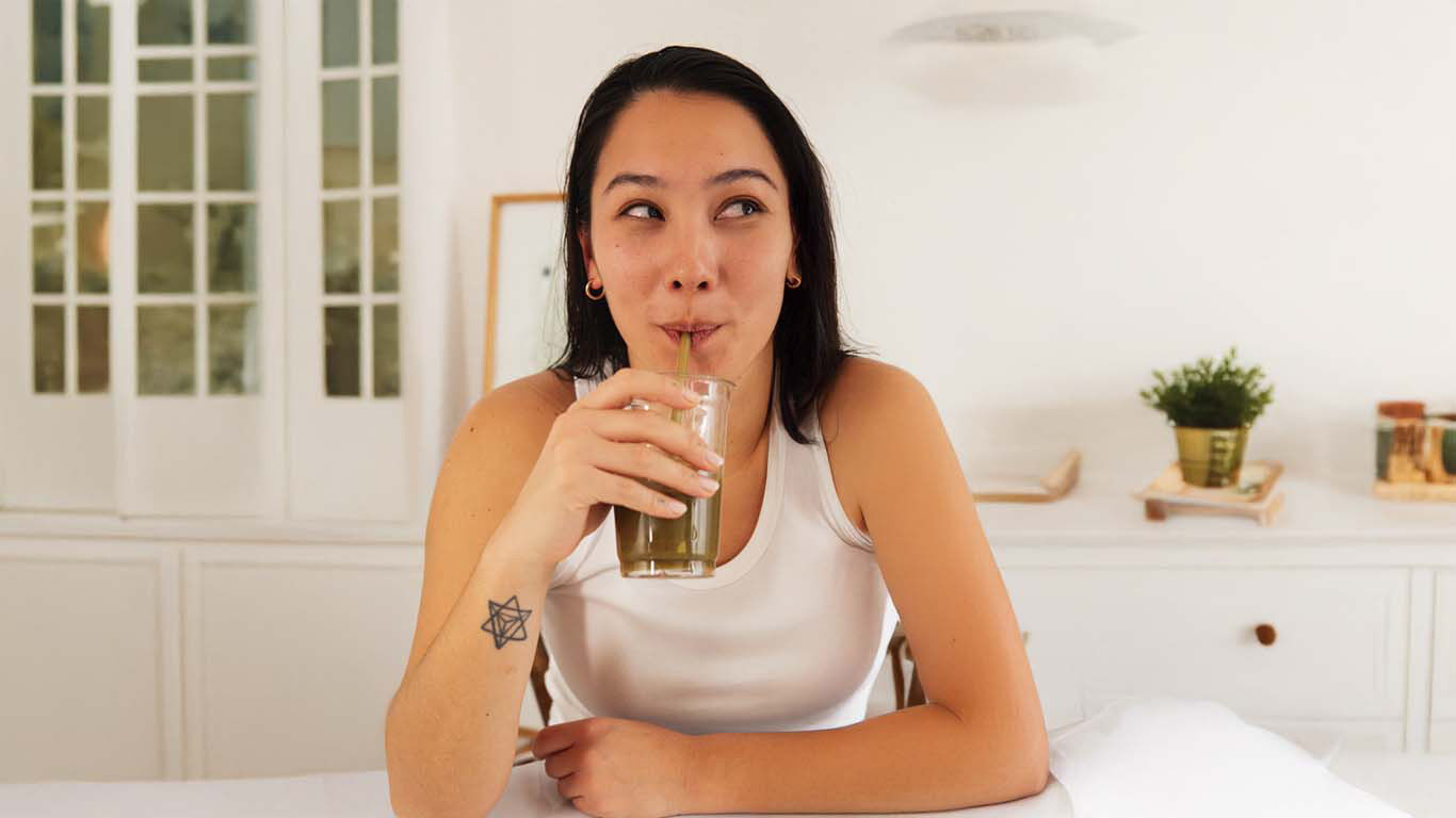 Frau trinkt gr&uuml;nen Smoothie in heller, gem&uuml;tlicher Wohnumgebung.