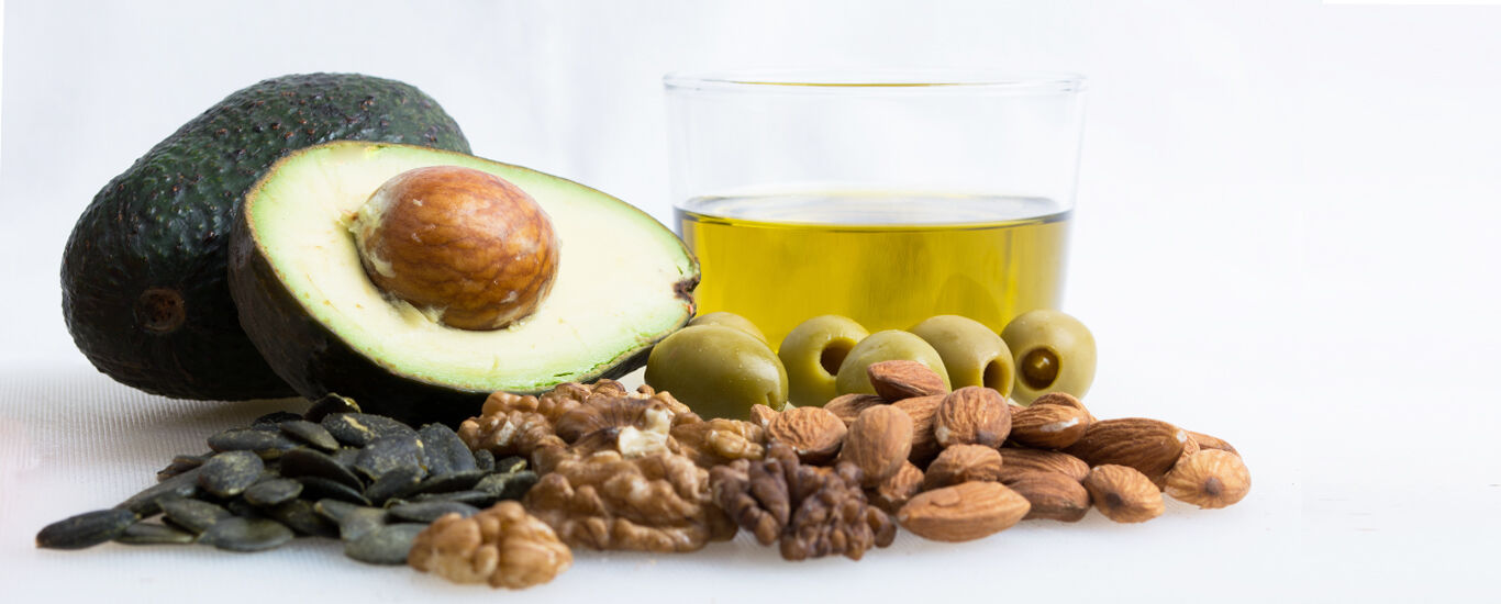 Aufgeschnittene Avokado, daneben Nüsse, Samen und Oliven sowie ein Glas mit Öl.