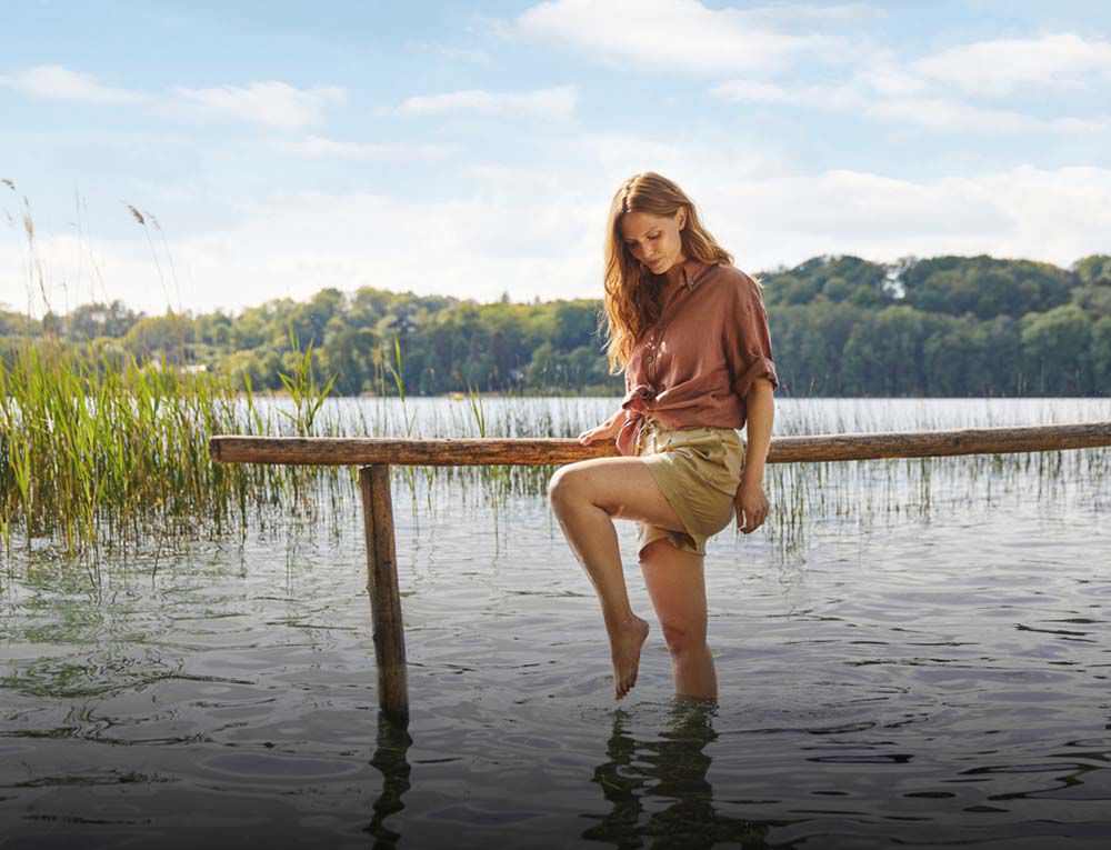 Frau l&auml;uft mit den F&uuml;&szlig;en durchs Wasser.