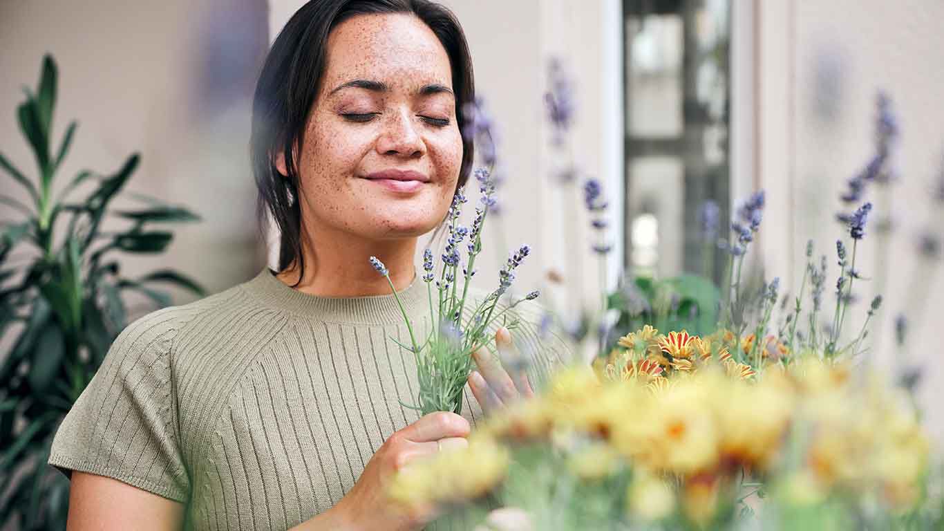 Frau erfreut sich über die Blumenpracht auf ihrem Balkon. In der Hand hält sie Lavendel.