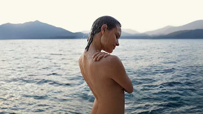 Frau steht nackt vor einem See.