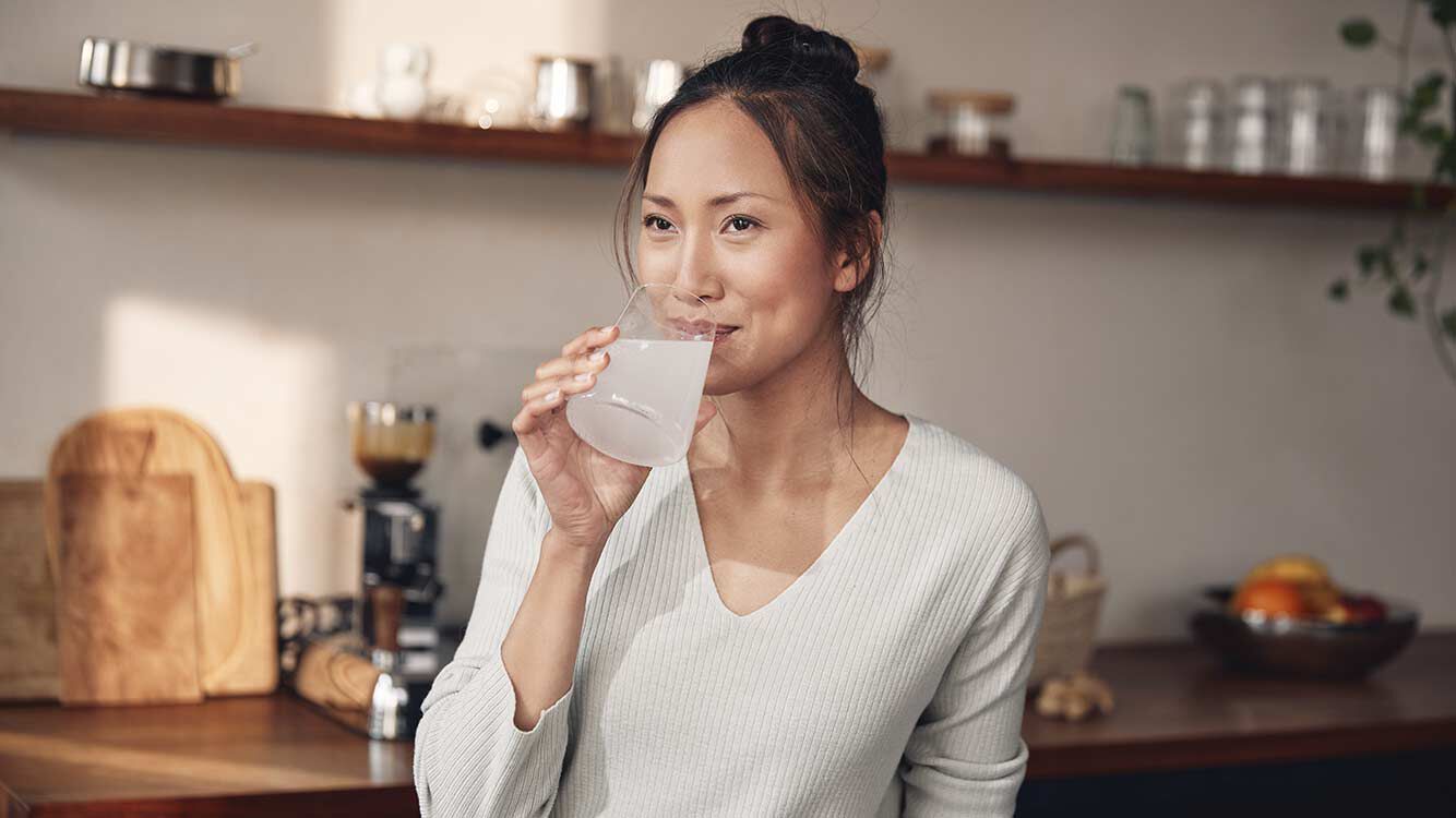 Magnesium und Calcium für gesunden Knochen Frau steht in der Küche und trinkt aus einem Wasserglas