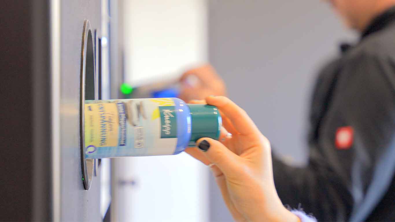 Hand steckt eine Kneipp Schaumbadflasche in einen Rückgabeautomaten.