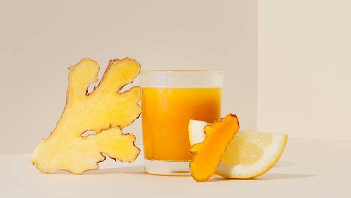 Gefülltes Glas mit Ingwer-Shot. Zutaten daneben: Ingwer, Kurkuma, Zitrone.