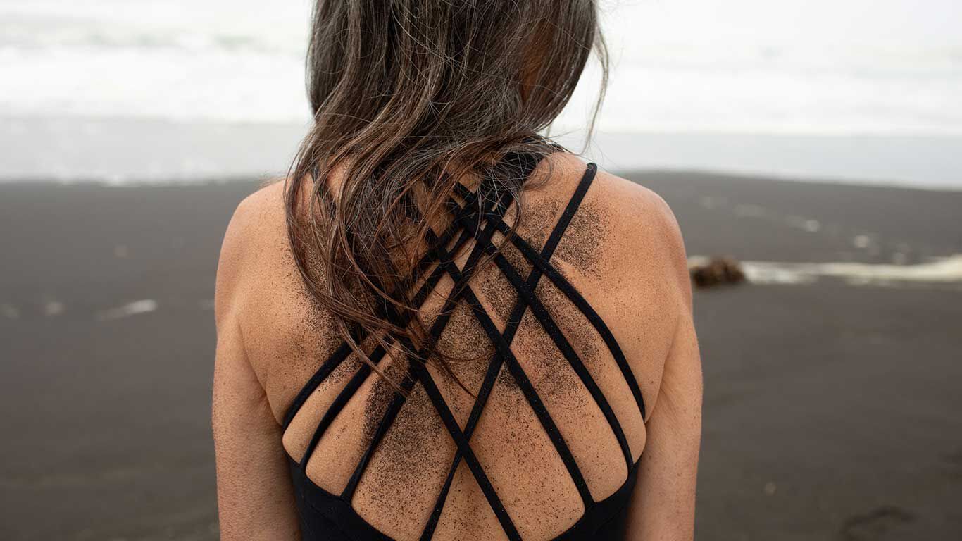 Rückenansicht einer Frau im Badeanzug. Rücken ist mit schwarzem Sand bedeckt.