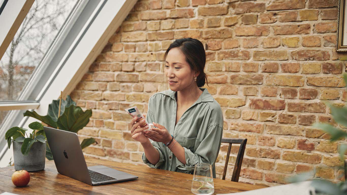 Frau sitzt mit einem Glas Wasser an einem Tisch vor einem ge&ouml;ffneten Laptop.