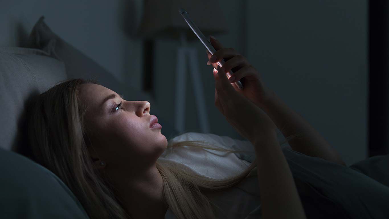 Frau liegt mit Handy im Bett