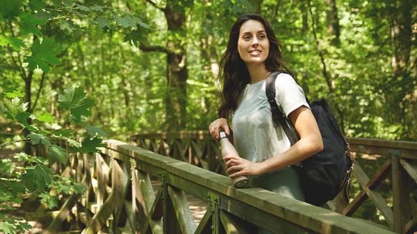 Frau macht an einer Holzbrücke im Wald Pause und genießt die Natur.