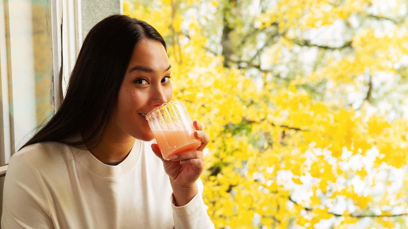 Frau genie&szlig;t ein Getr&auml;nk am Fenster mit herbstlicher Aussicht.
