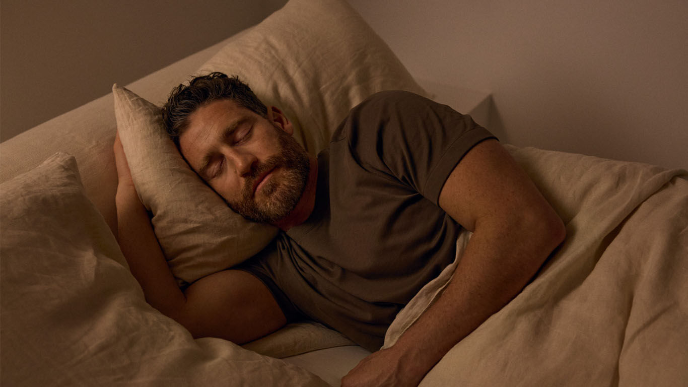 Mann liegt zugedeckt im Bett und schl&auml;ft.