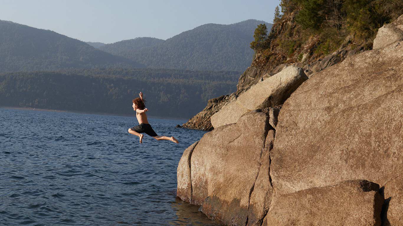 Junge springt von einem Felsen in das Meer.