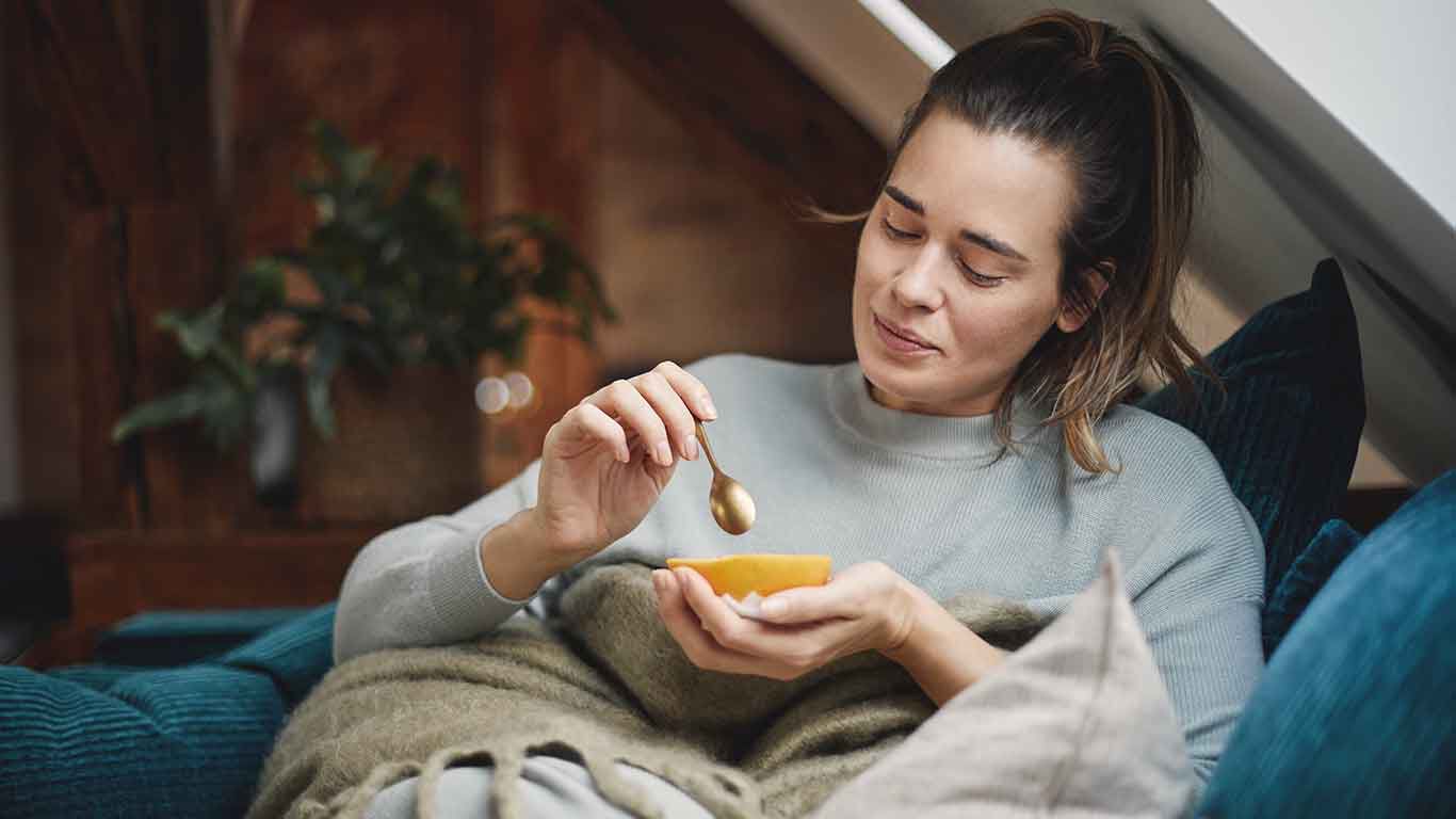 Frau sitzt auf Couch und löffelt Grapefruit.